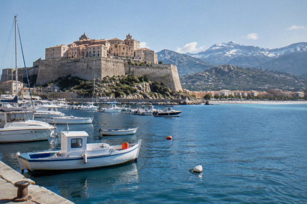 Boats moored in Calvi harbour beneath the old stone walls of the citadel in Corsica