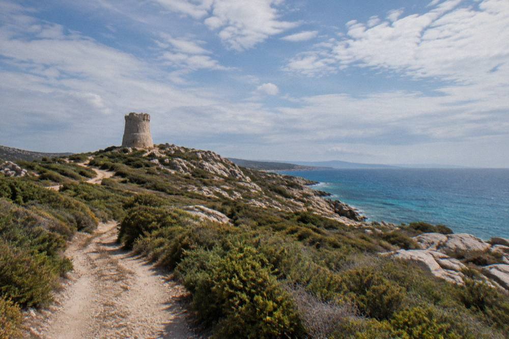 A stone watchtower on a headland above maquis and open sea