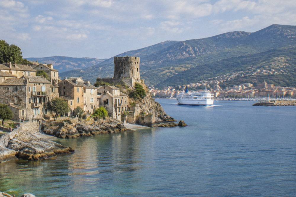 A white ferry ship entering a busy Mediterranean harbour town with hills behind