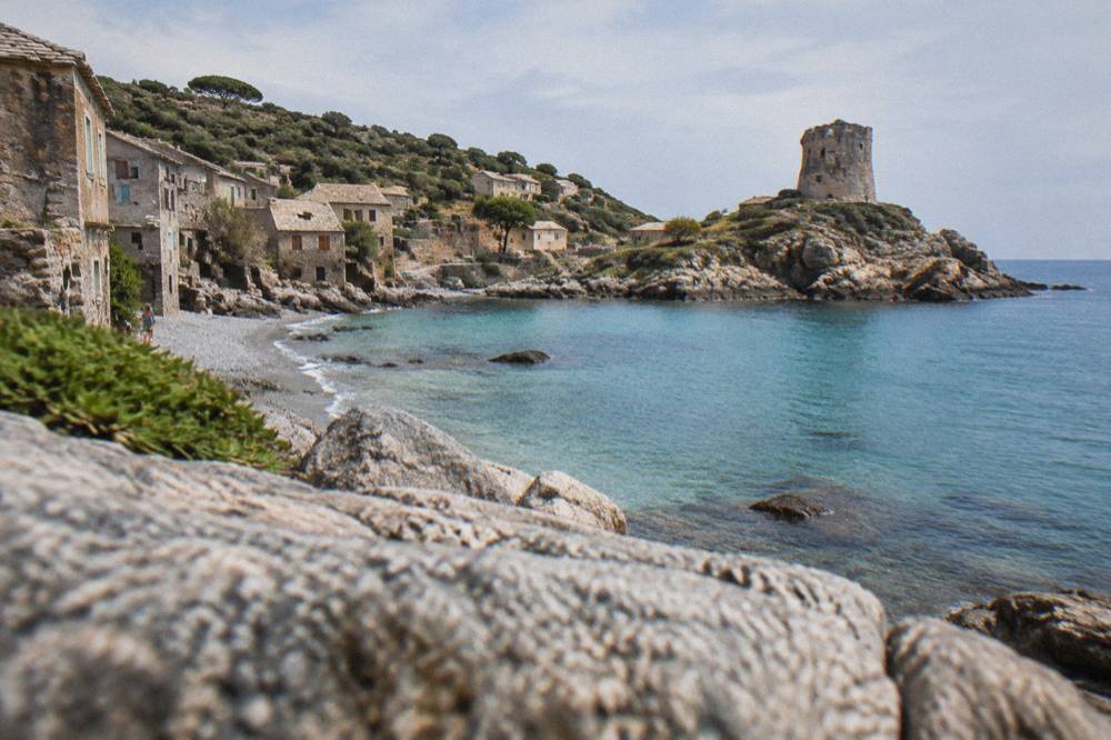 A turquoise Mediterranean cove with a pebble shore and low green scrub on the hillsides