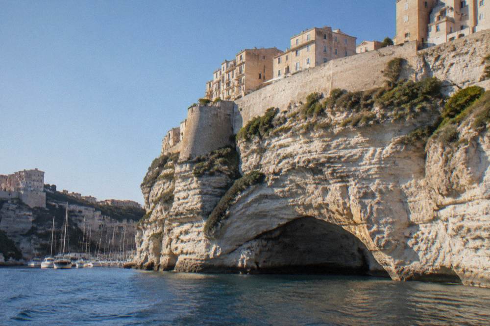 The cliffside town of Bonifacio seen from the water with tall white walls above a cave arch