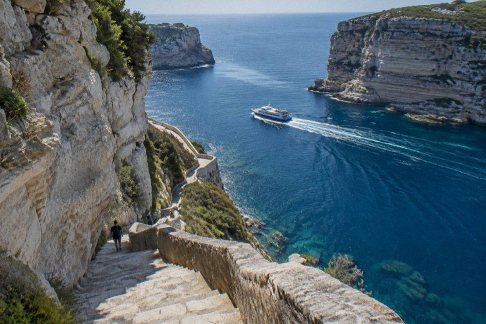 A ferry passing between steep cliffs on a short sea crossing in bright light