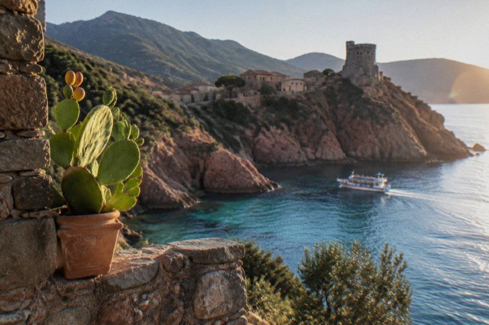 Red granite cliffs dropping into clear water with a passing excursion boat below