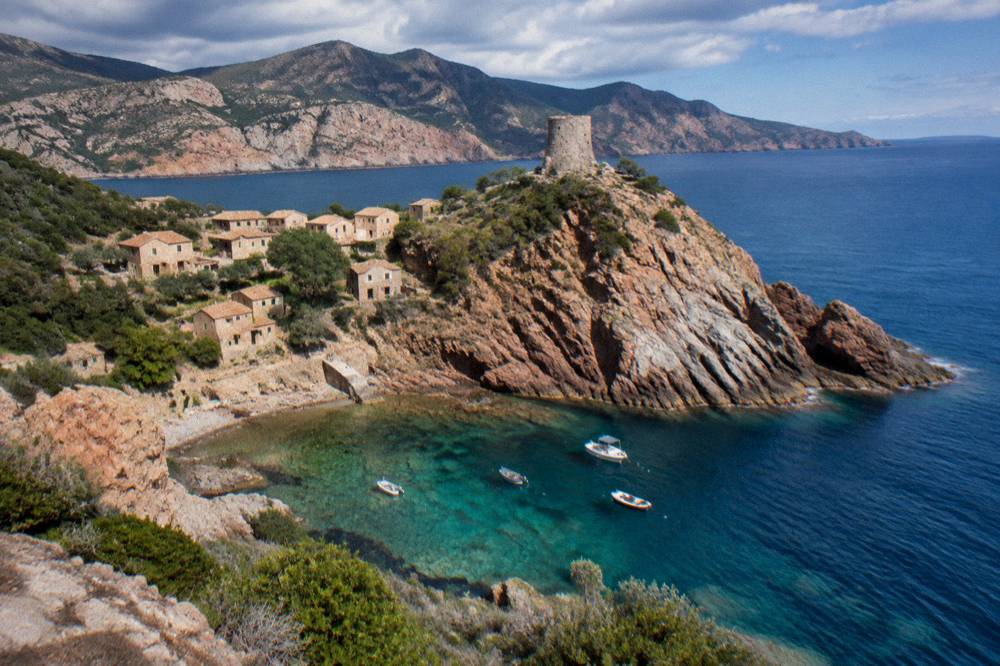Rocky headland rising from blue sea with layers of red and grey stone visible in the cliff face