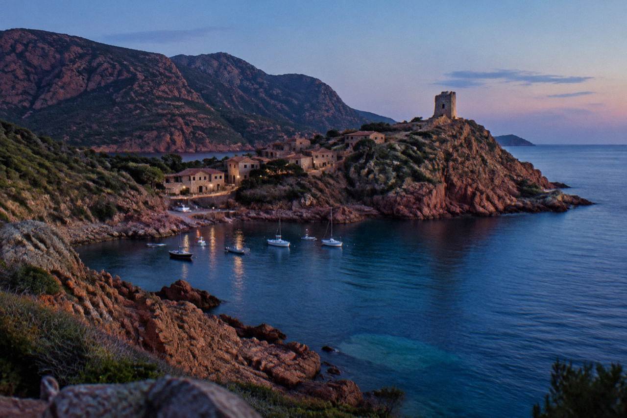 Red granite cliffs rising above a calm blue sea on the Corsican coast