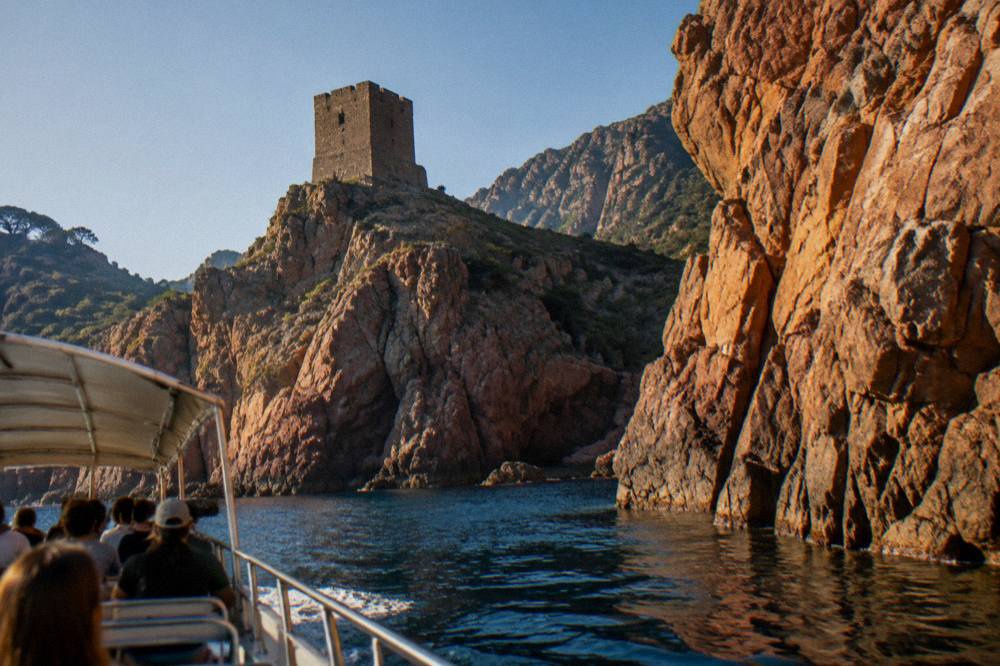An open excursion boat passing close under tall red rock walls