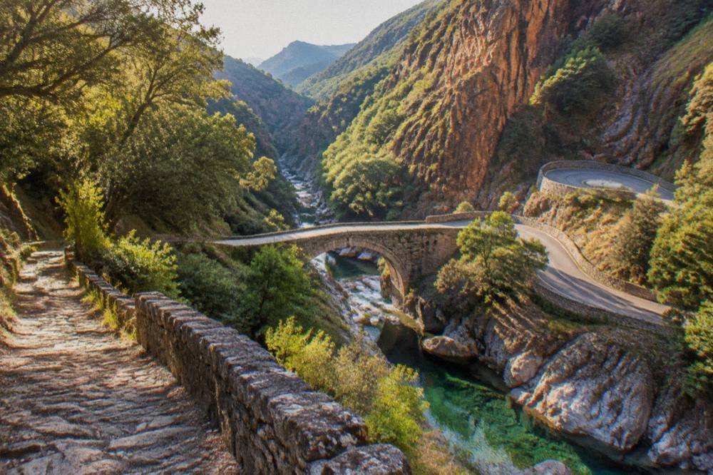 A mountain road with hairpin bends descending towards a river gorge