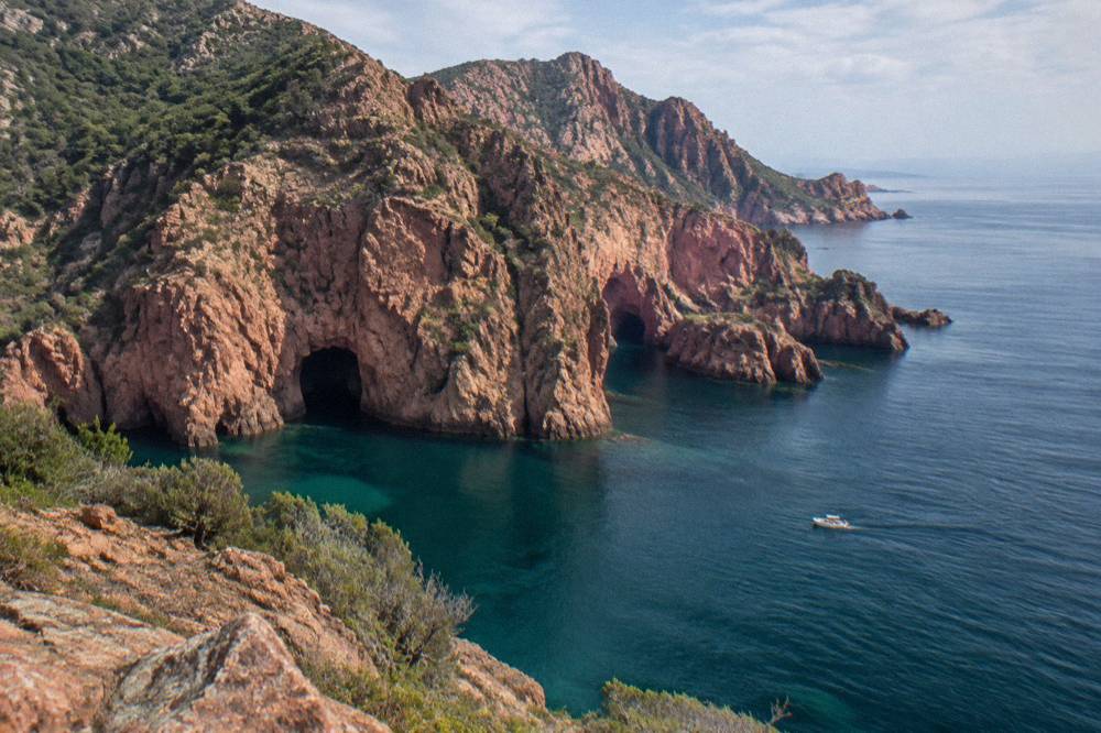 Red granite cliffs rising above calm sea near a coastal village