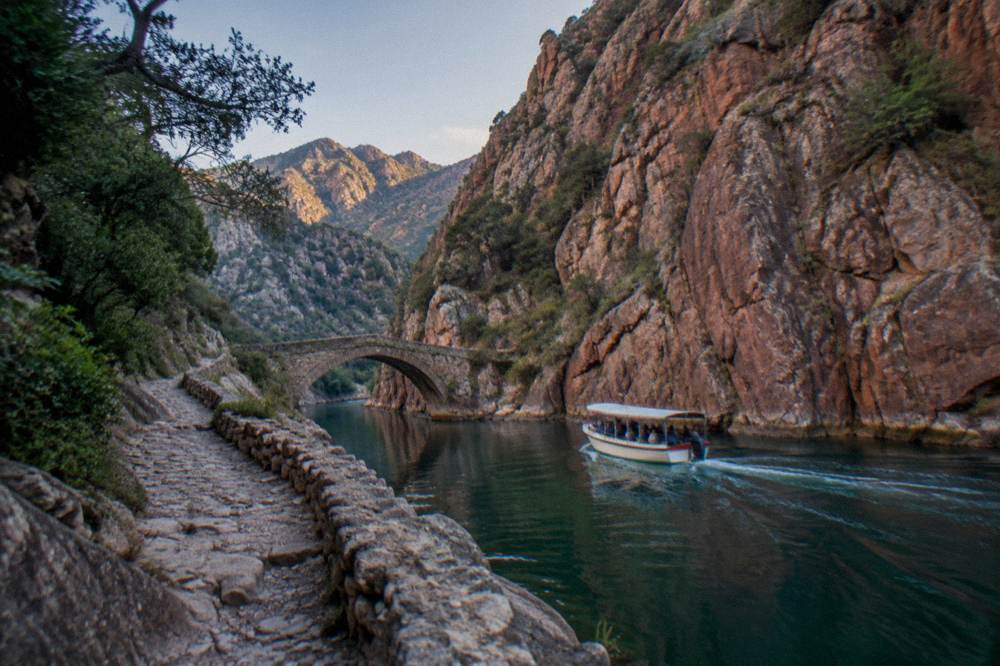 A boat cruising close to tall red rock cliffs at the waterline