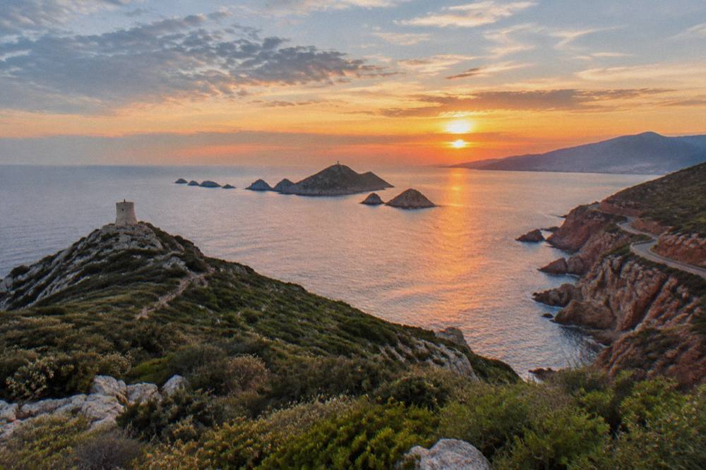 A winding coast road above the sea with red cliffs and distant mountains
