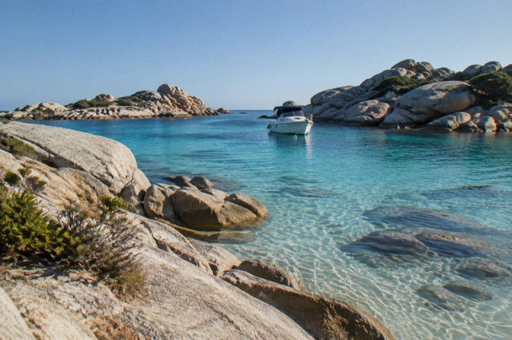 A boat anchored in a turquoise channel between granite islets of the Lavezzi archipelago