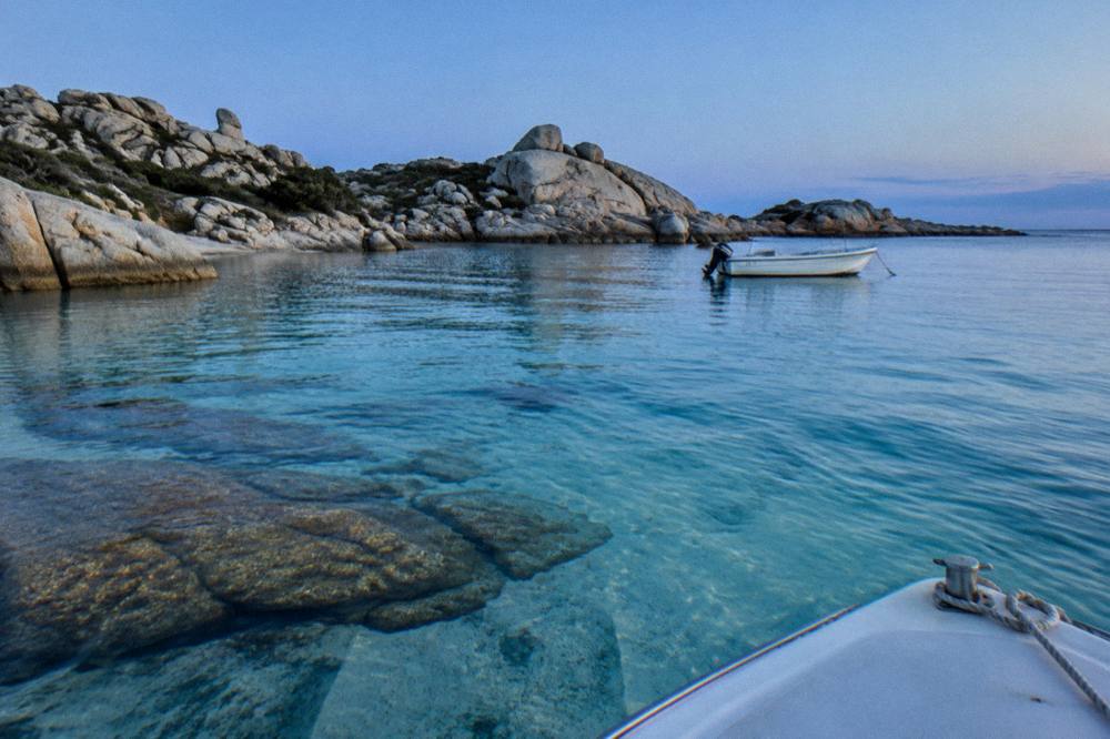 Clear water over pale sand and granite near the bow of a small boat at the Lavezzi islands