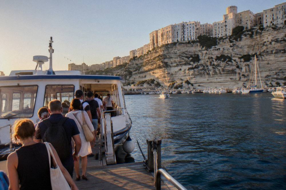 Passengers boarding a tour boat at a wooden pontoon in Bonifacio harbour
