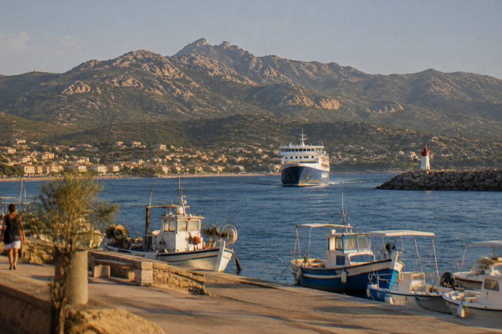 A ferry approaching a harbour on the coast of Corsica in daylight