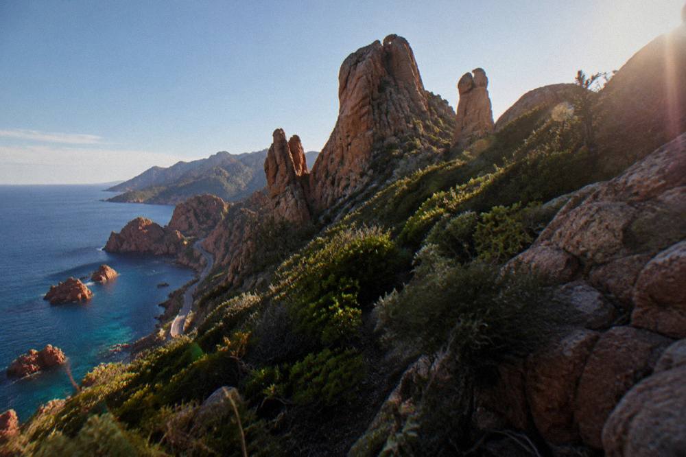 Red granite rock formations rising from clear water along the coast of western Corsica