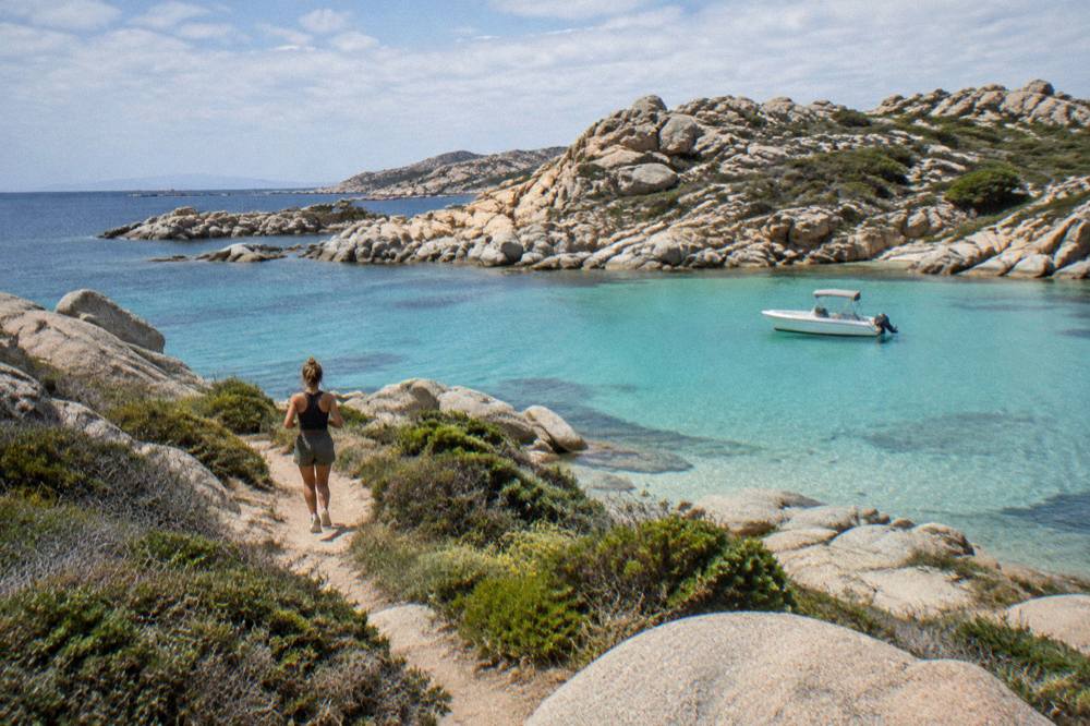 A small boat anchored in a turquoise cove below rocky hills on the Corsican coast