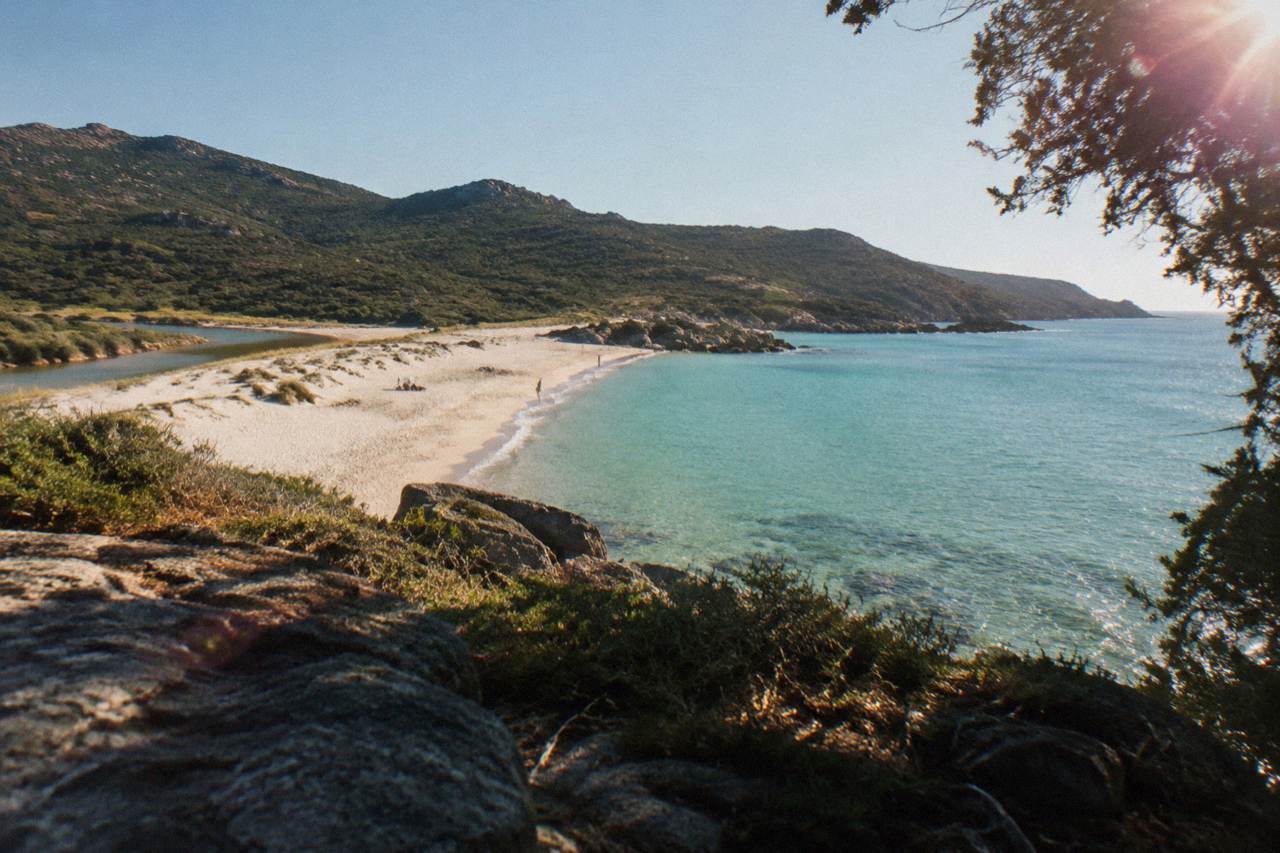 A long sandy beach curving between green hills and calm turquoise sea under a clear sky