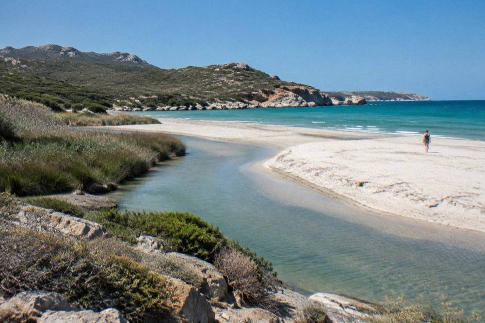 A river winding through sand and reeds toward the sea behind a beach