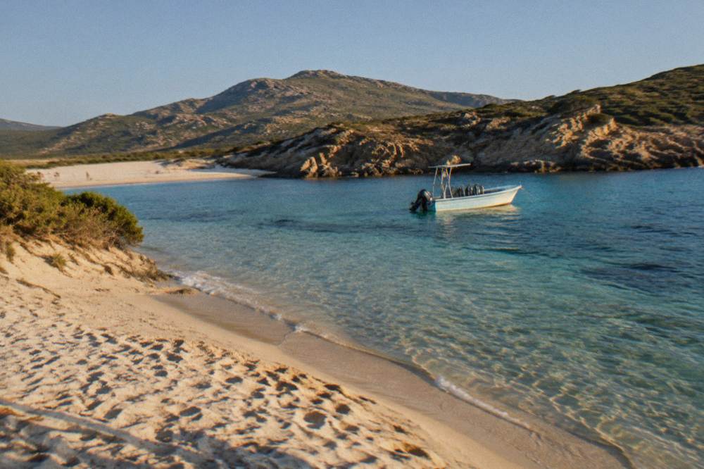 A small diving boat anchored over clear shallow water near a rocky point