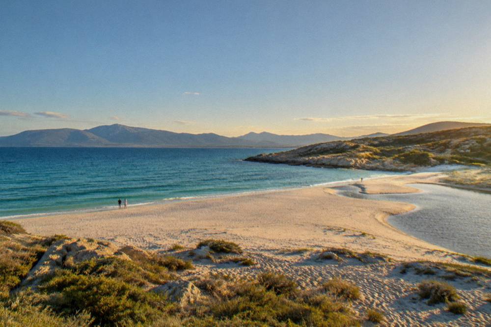 Golden evening light across a wide bay with distant mountains along the horizon
