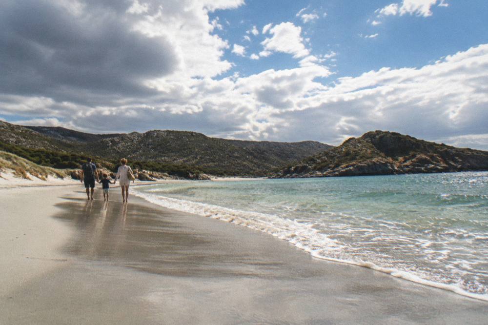 A family walking along the wet sand at the edge of gentle waves