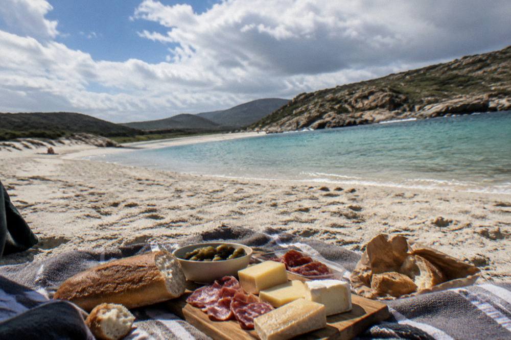 A picnic spread of cheese, charcuterie and bread on a towel beside a beach