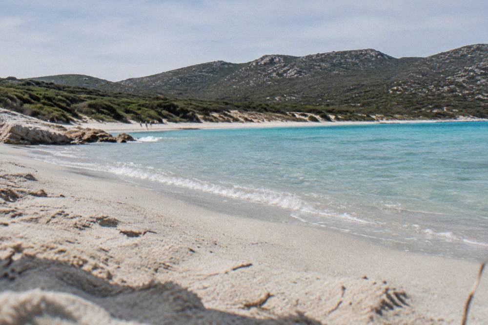 Turquoise sea breaking gently on the sand of a southern Corsican beach with maquis covered hills behind