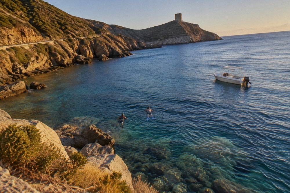 Snorkelers in the water beside a small boat above rocks and clear sea near the Corsican coast