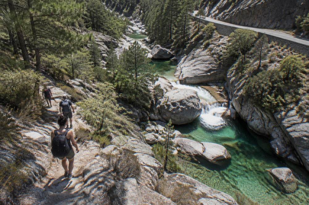 Hikers with backpacks on a rocky mountain path above a river gorge