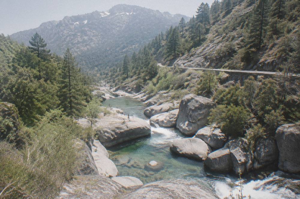 A granite mountainside with patches of old snow above a green valley