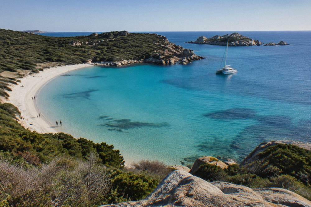A catamaran anchored near small granite islands in clear blue sea