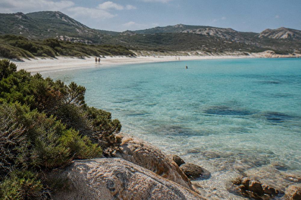 Turquoise shallows over pale sand with low green hills behind the beach