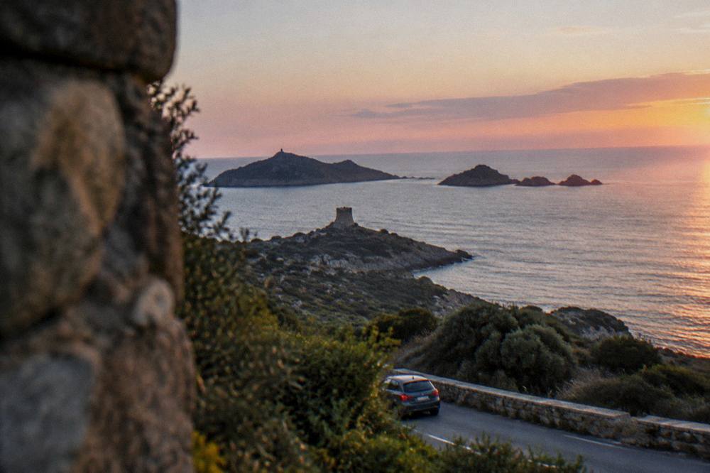 A coastal road scene in southern Corsica with maquis-covered hills near the shore.