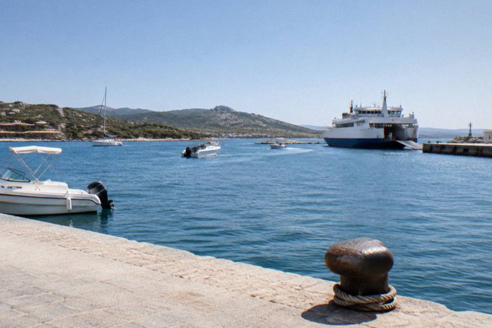 A ferry and small boats in a southern Corsican harbour near beaches and low hills.