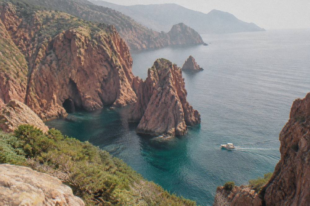 Dark red volcanic cliffs and sea caves along a wild roadless coast with a small boat far below