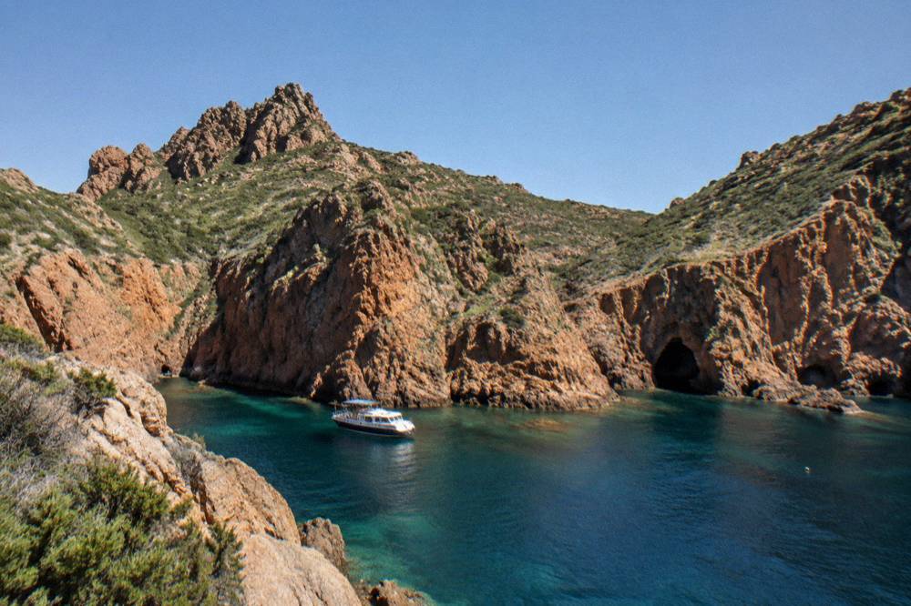 A small cruise boat moored in a rocky cove with orange cliffs behind it