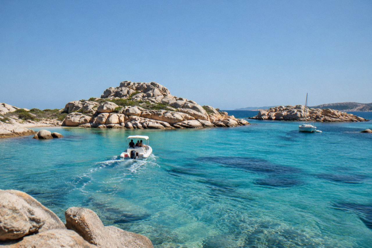 A boat crossing clear water toward granite islands off the southern tip of Corsica