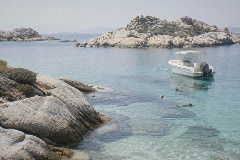 Snorkellers in the water beside a moored boat near small granite islands