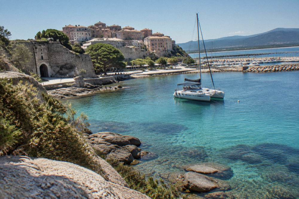 A catamaran moored near granite rocks in a clear turquoise lagoon