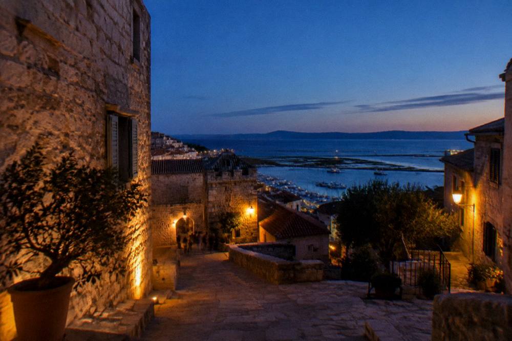 An old town street with stone buildings leading towards a sea horizon at dusk