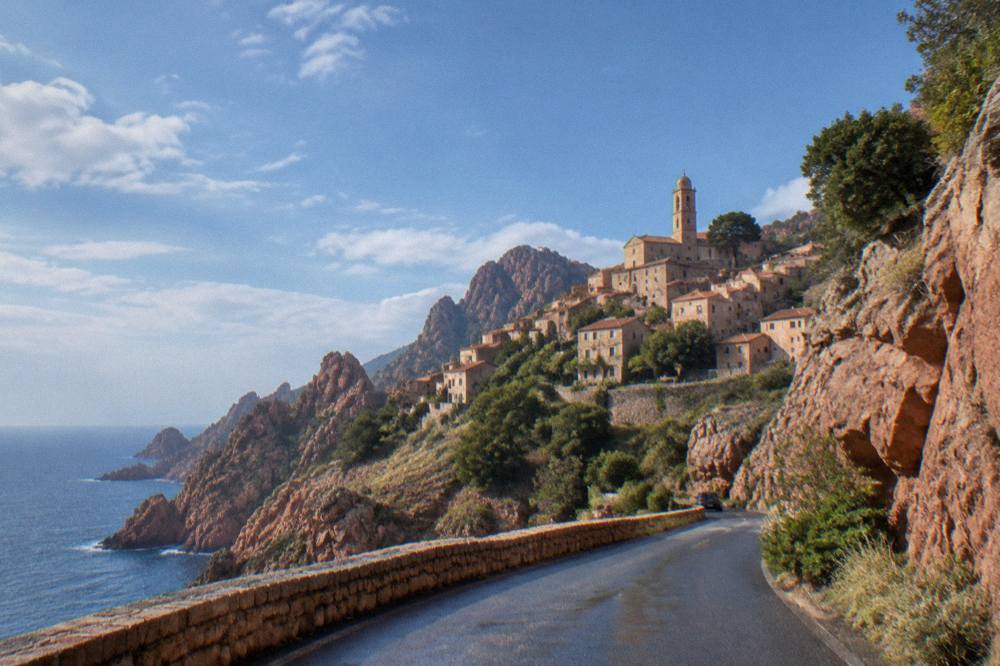 A winding coastal road cut into red rock above the sea near Piana