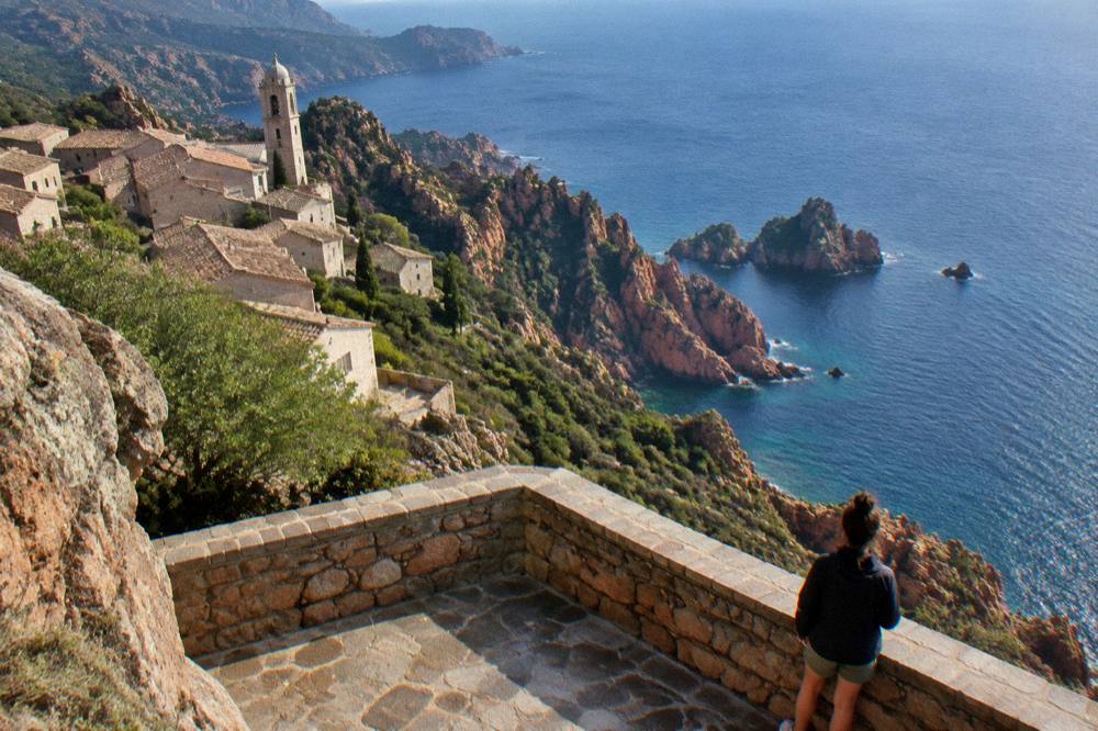 A stone viewpoint terrace above red rocks and blue sea on the Piana coast