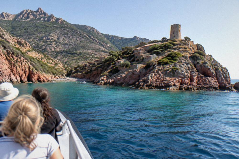 Passengers on a small cruise boat approaching a rocky cove from the sea