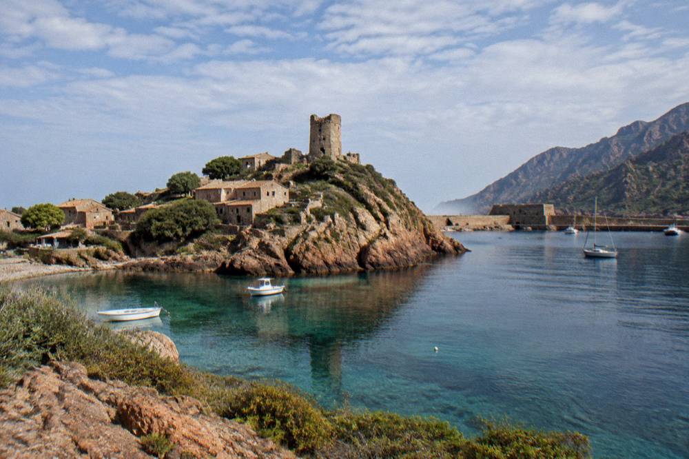 A calm morning sea with a town harbour and a fortress wall in the background