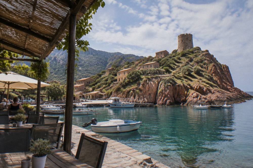 A shaded café terrace beside a small harbour with boats moored alongside