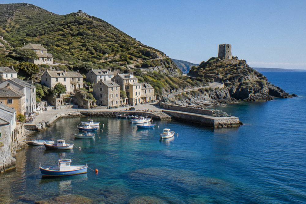 A small stone harbour village on the Cap Corse coast with fishing boats moored in clear water
