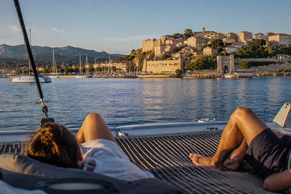 Passengers relaxing on the bow netting of a catamaran at anchor