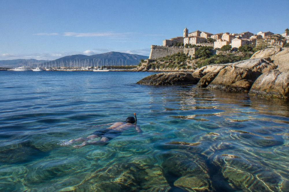 A snorkeller swimming over rocks in clear shallow sea