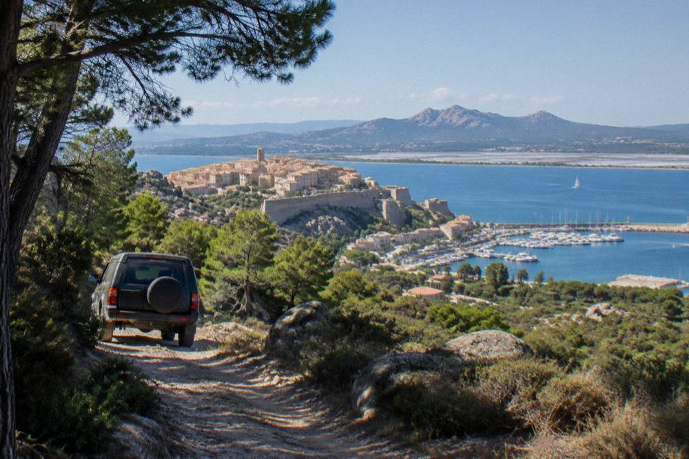 A 4x4 vehicle on a mountain track among pine forest and granite peaks