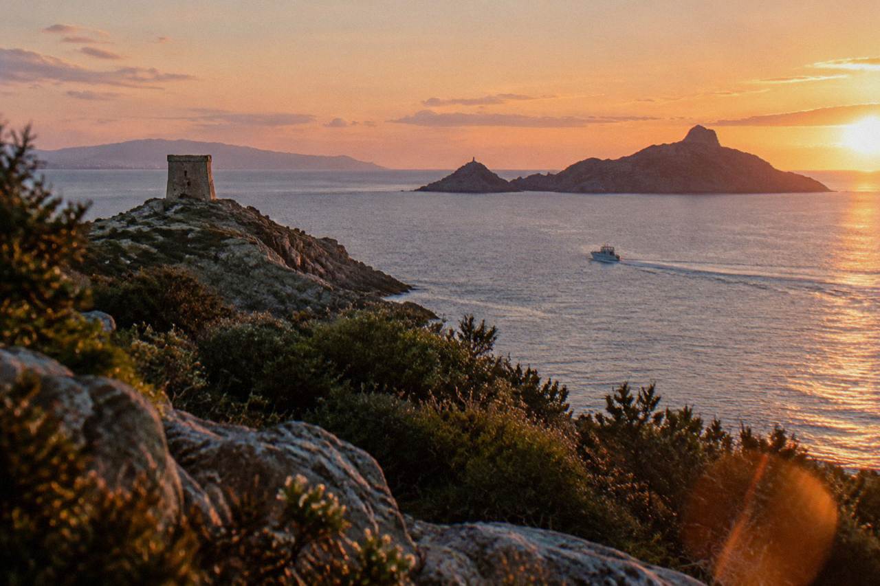 A small boat crossing the Gulf of Ajaccio towards red granite islands under an evening sky